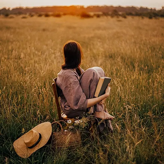 kobieta z książką siedząca na krześle w polu podczas zachodu słońca